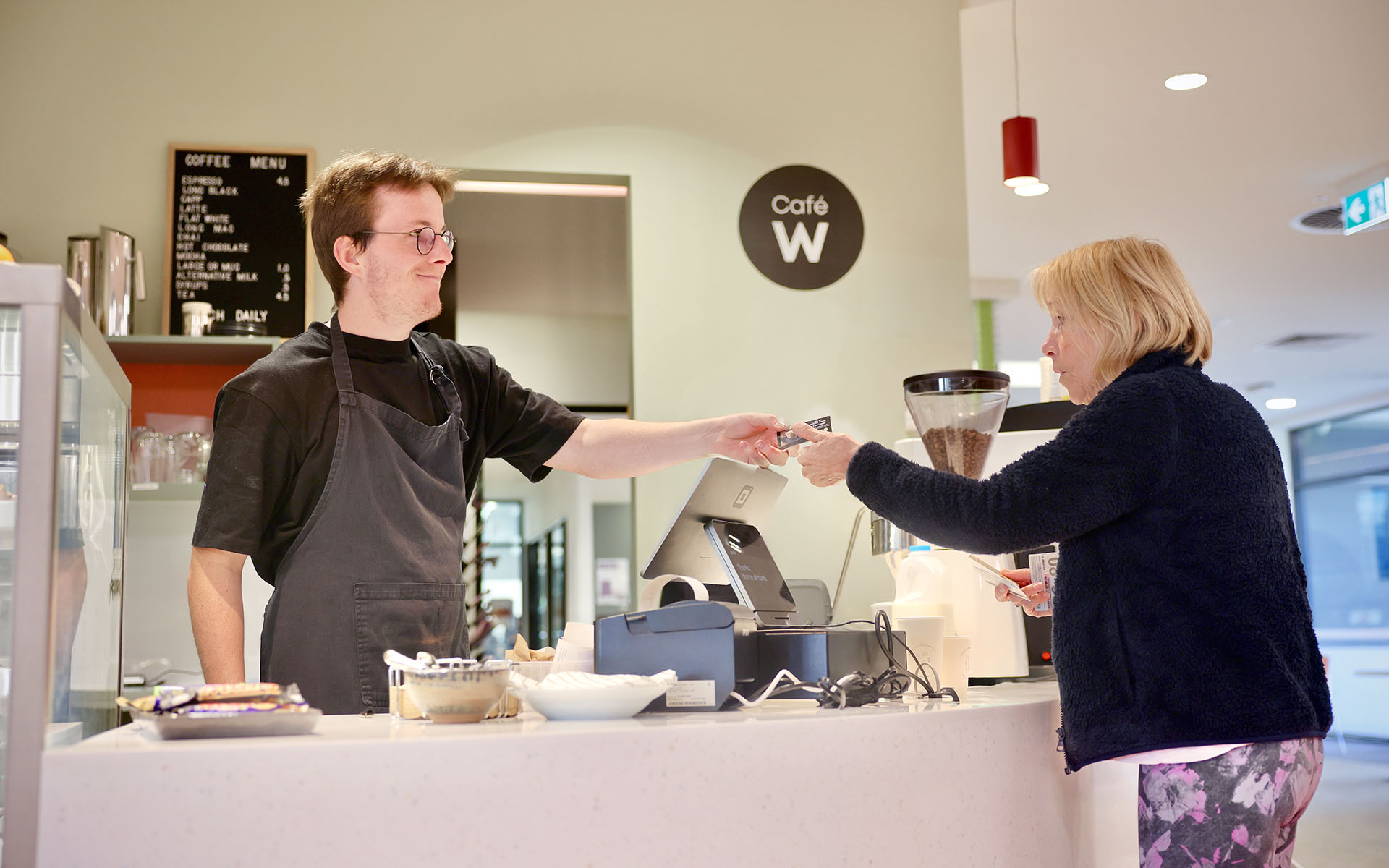A Wallara participant serving a customer at a café counter.