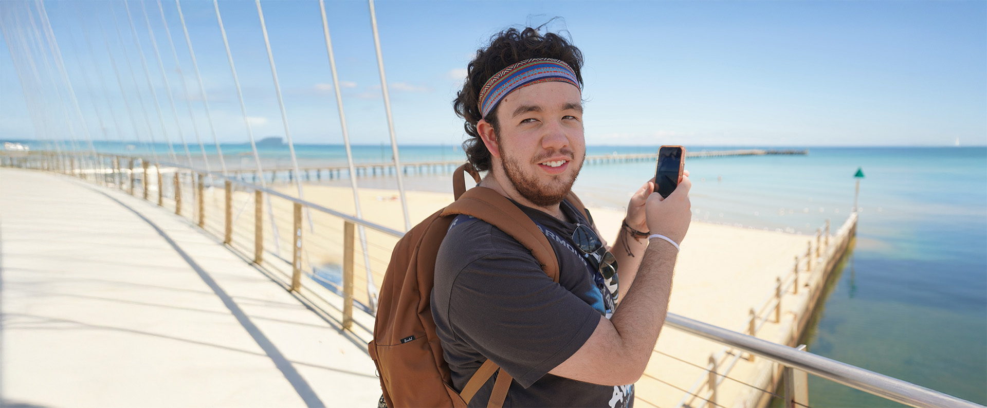 A Wallara participant taking a photo on a phone, outdoors by the ocean.