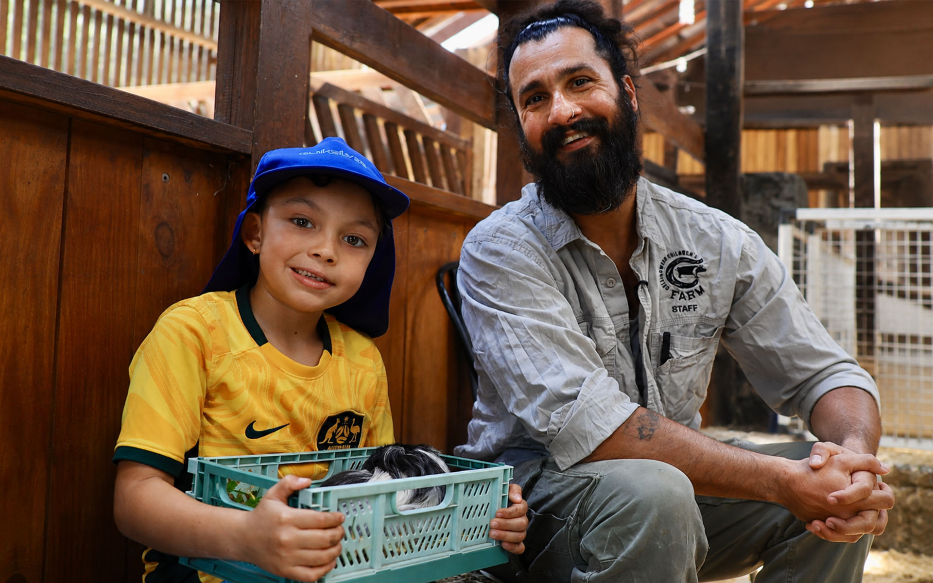 A child holding a container with guinea pigs beside a Collingwood Children’s Farm staff member.