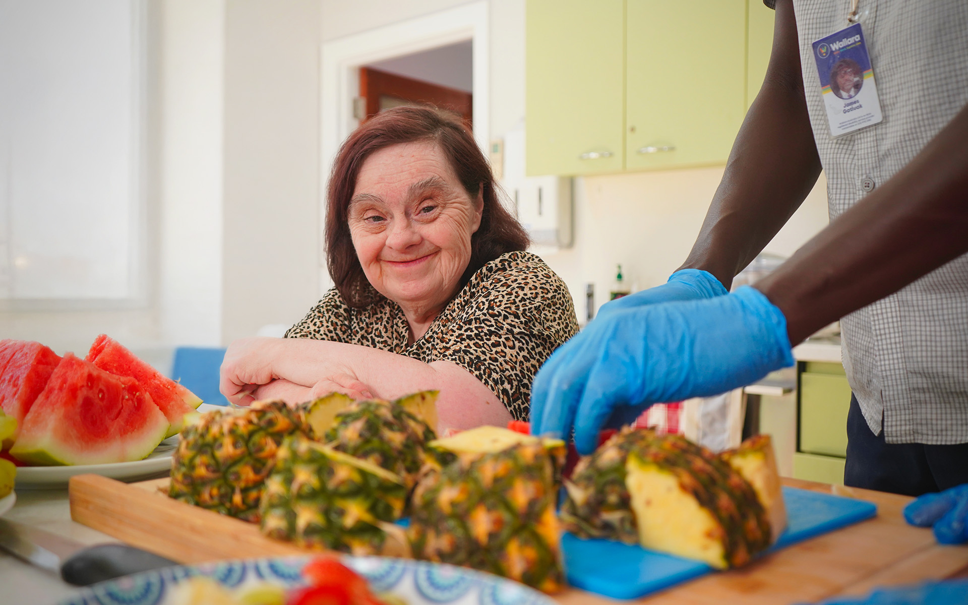 A Wallara participant preparing fruit with support from a staff member in a kitchen.