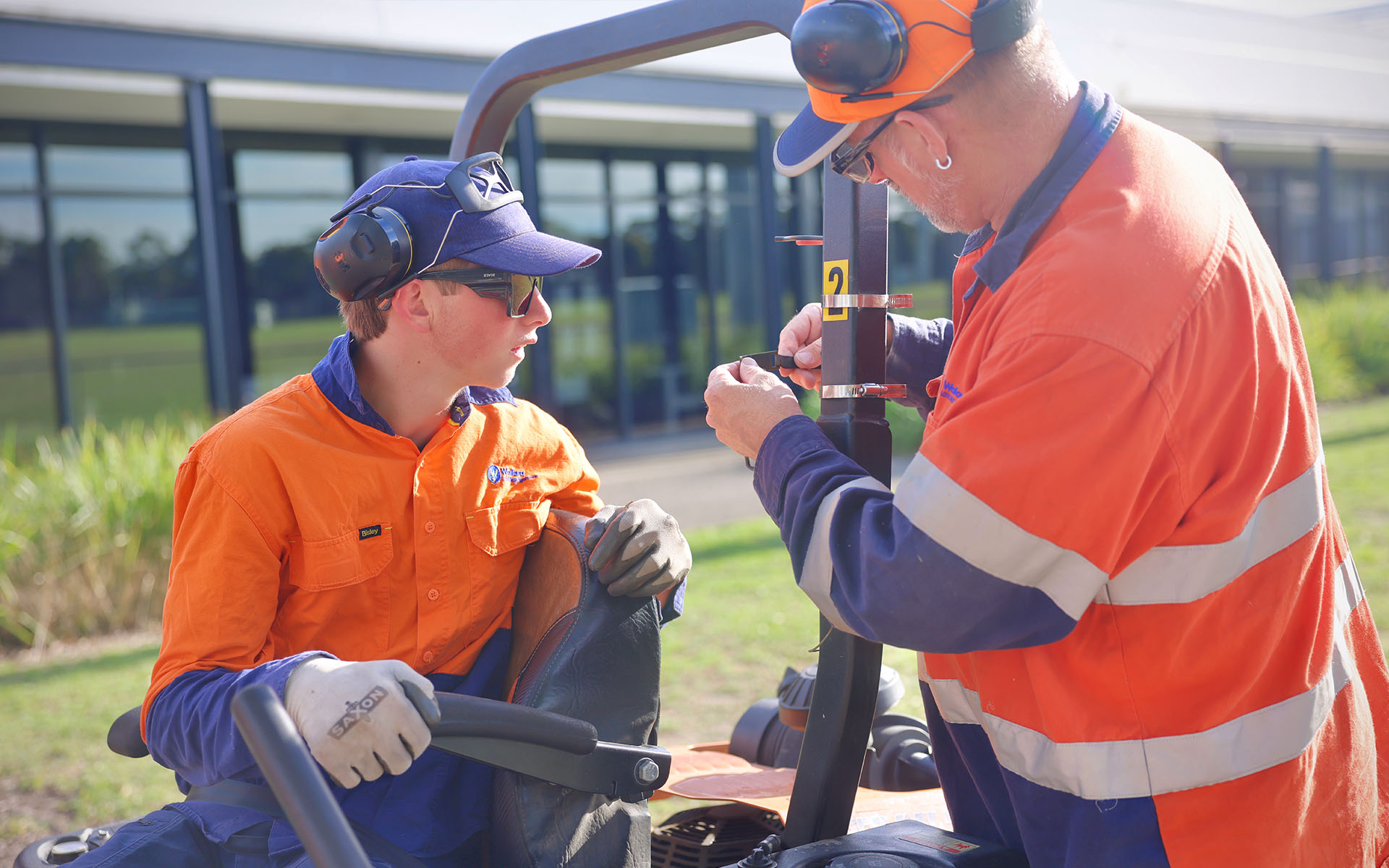 A Wallara participant receiving support from staff member on a rode on mower during outdoor maintenance work.