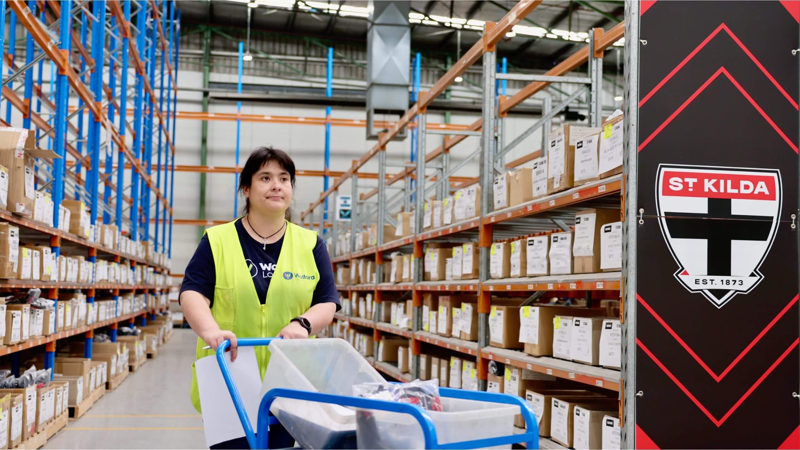 A Wallara participant pushing a trolley through a warehouse aisle.