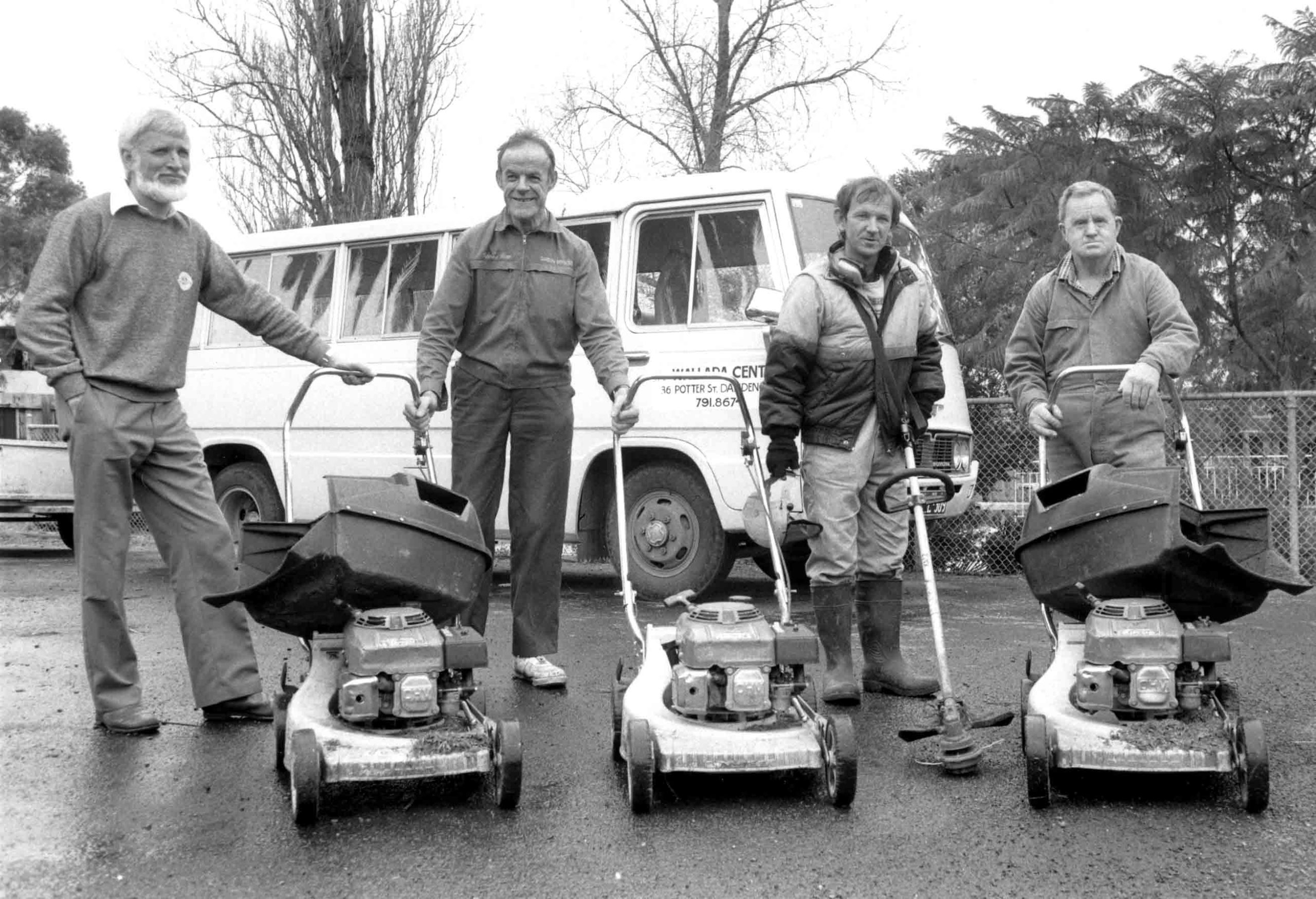 Wallara participants and staff standing together with lawn mowers during the early years of the organisation.