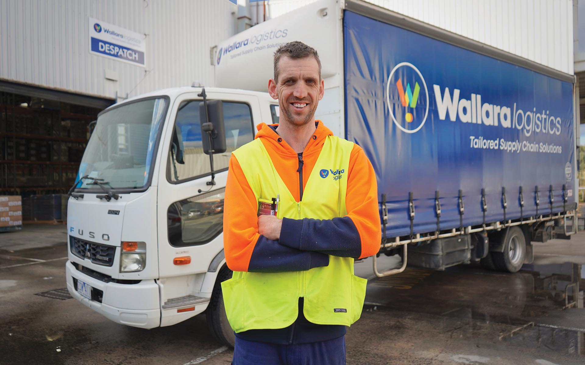 A Wallara participant stands in front of a Wallara Logistics delivery truck while wearing a high-visibility work uniform.