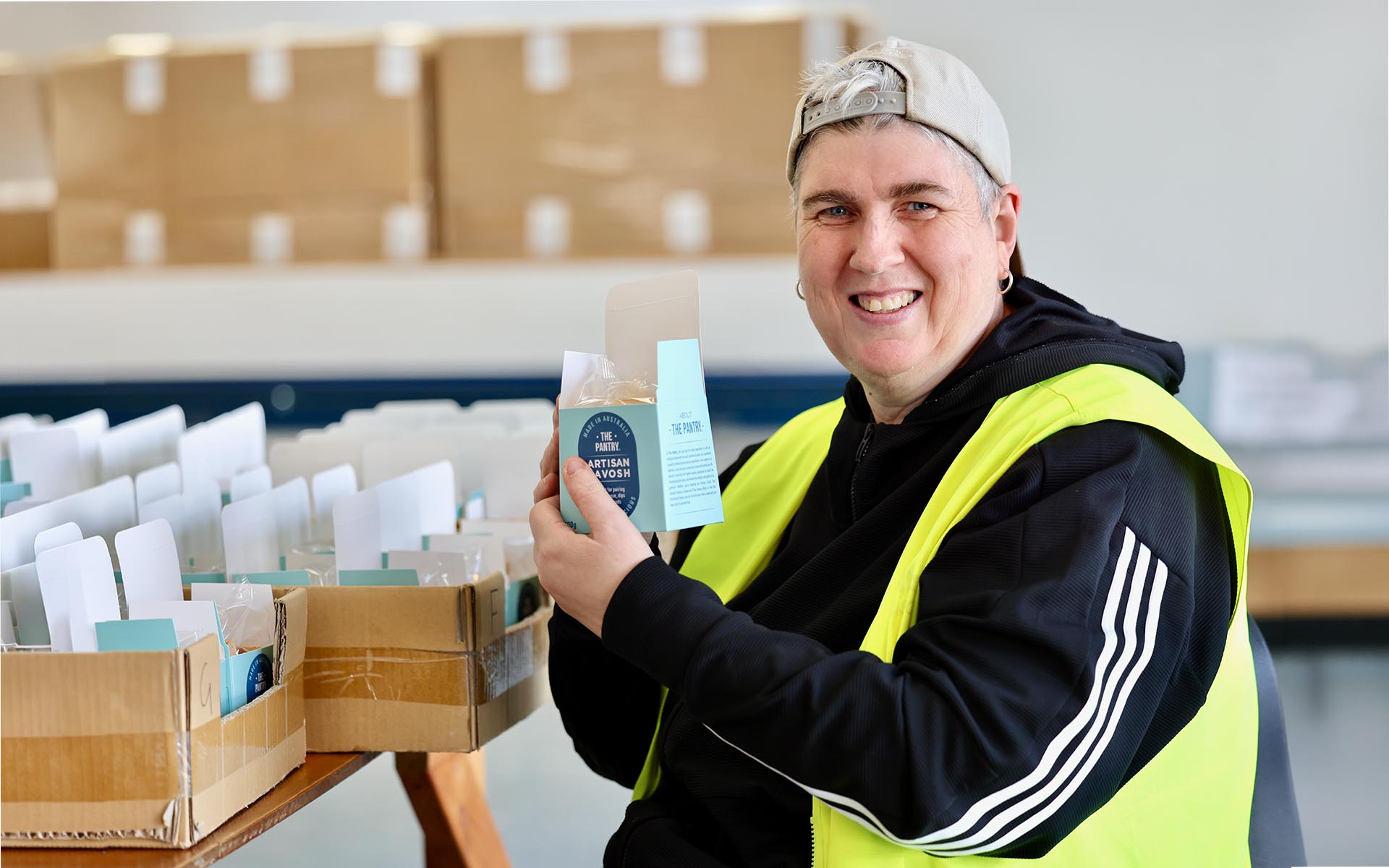 A Wallara participant packs products into boxes at a workstation in a supported employment setting.